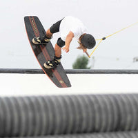 Person wearing white shirt and black helmet is doing a wakeboard trick on a horizontal pole